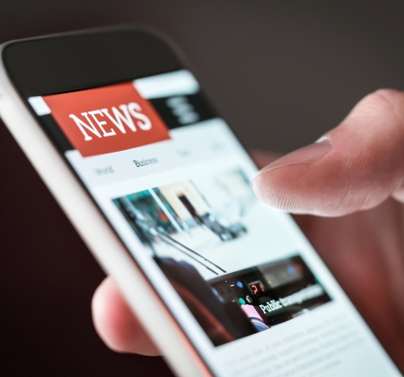 A hand holding a phone with a website displayed and the headline is News