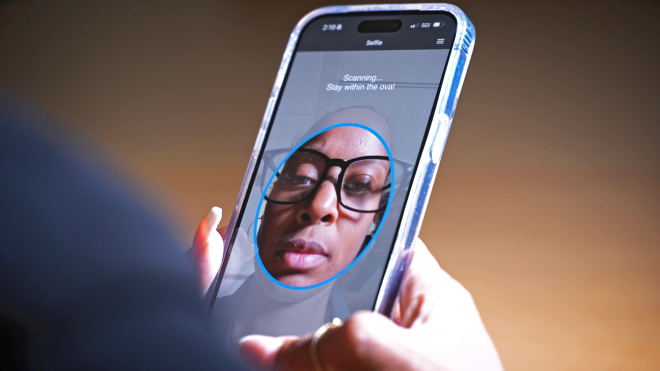 Phone screen of person taking selfie for MiD enrollment. Text on screen says "scanning... stay within the oval".